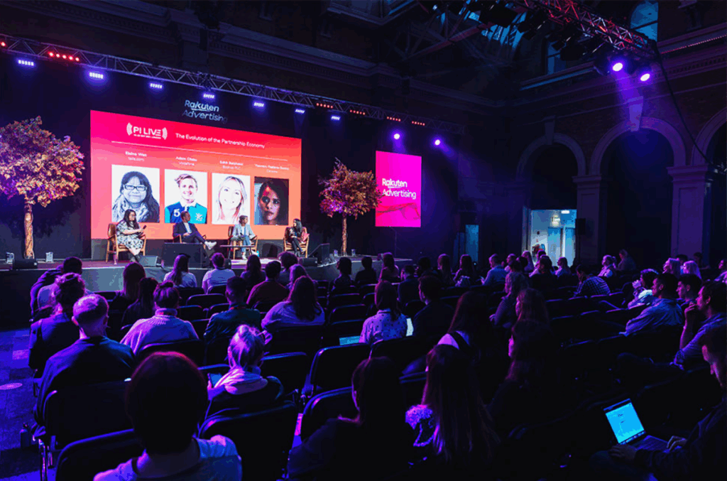 An image of the panelist discussion on stage and attendees listening during the PI LIVE conference